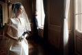 elegant gorgeous bride gently looking under veil at stylish groom standing at window light, holding calla bouquet. unusual