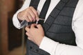 Elegant gorgeous groom getting ready in the morning in the hotel room, holding clip on his tie. Royalty Free Stock Photo