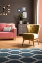 Elegant green armchair and a blue rug with pattern on hardwood floor in a dark gray living room interior with a pink sofa.