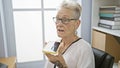 Elegant grey-haired senior woman sending voice message via smartphone at her office job, the successful, concentrated boss Royalty Free Stock Photo