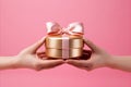 Elegant hand showcasing a beautifully wrapped gift box on a soft pink background Royalty Free Stock Photo