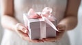 Elegant hands presenting a gift box with a soft pink satin ribbon, conveying a sense of care and celebration for a special moment