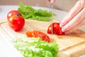 Elegant hands of a young girl cut juicy red tomato into halves on a wooden cutting board. Preparation of ingredients and Royalty Free Stock Photo