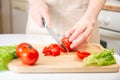 Elegant hands of a young girl cut juicy red tomato into halves on a wooden cutting board. Preparation of ingredients and Royalty Free Stock Photo