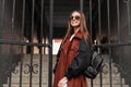 Elegant happy young hipster woman with smile in stylish sunglasses in fashionable trench coat with trendy leather black backpack Royalty Free Stock Photo