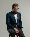 elegant high class man with glasses looking down and sitting with hand in pocket Royalty Free Stock Photo