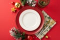 Top view of plates, golden flatware, napkin, wine glass, ornaments, confetti, frosted fir, mistletoe on crimson backdrop