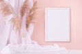 Elegant home decoration - blank photo frame for poster hanging on pink wall, curtain, beige fluffy reeds on white wooden shelf. Royalty Free Stock Photo