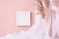 Elegant home decoration - square blank photo frame hanging on pink wall, curtain, beige fluffy reeds in vase. Contemporary simple. Royalty Free Stock Photo