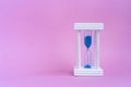 Elegant hourglass with running blue sand on pink background