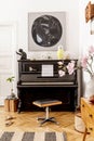 Elegant interior of living room with black piano, furniture, plant, flower, wooden clock, lamp, mock up painitngs, decoration. Royalty Free Stock Photo