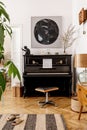 Elegant interior of living room with black piano, furniture, plant, flower, wooden clock, lamp, mock up painitngs, decoration. Royalty Free Stock Photo