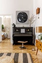 Elegant interior of living room with black piano, furniture, plant, flower, wooden clock, lamp, mock up painitngs, decoration. Royalty Free Stock Photo