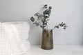 Elegant interor still life. Amber glass vase with bouquet of dry eucalyptus tree branches on white table, night stand