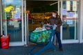 An elegant italian man wearing COVID-19 protection mask exiting grocery store with shopping cart stocked up with essentials