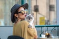 Elegant Italian woman with hat and glasses kisses her cat