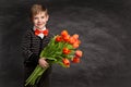 Elegant Little Boy presenting Flowers. Happy Smiling Child holding Bouquet over Chalk Blackboard. Fashion Stylish Kid with Tulips Royalty Free Stock Photo