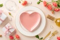 Top view heart-shaped plate, cutlery, white wine bottle. Graceful roses, gift boxes, themed decor enhance beige ambiance