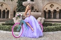 Elegant luxury fashion. Glamour, stylish elegant woman in amazing long gown dress on colorful bike. Female model in lilac long Royalty Free Stock Photo