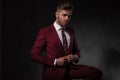 Elegant man buttoning his red suit while sitting Royalty Free Stock Photo