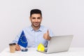 Elegant man sitting at workplace with paper house and European Union flag, showing thumbs up, like gesture