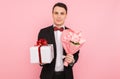 Elegant man, in a suit, with a bouquet of flowers, and a gift box, on a pink background, the concept of women`s day Royalty Free Stock Photo