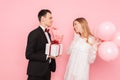 Elegant man in a suit, gives a box with a gift and a bouquet of flowers, to a beautiful woman, on a pink background. Women`s day Royalty Free Stock Photo