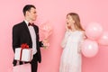 Elegant man in a suit, gives a box with a gift and a bouquet of flowers, to a beautiful woman, on a pink background. Women`s day Royalty Free Stock Photo