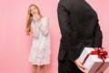 Elegant man in a suit makes a surprise to a woman, gives a bouquet of flowers and a box with a gift, on a pink background Royalty Free Stock Photo