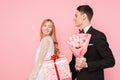 Elegant man in a suit makes a surprise to a woman, gives a bouquet of flowers and a box with a gift, on a pink background Royalty Free Stock Photo