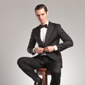 Elegant man in tuxedo buttoning his coat while sitting Royalty Free Stock Photo