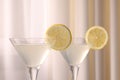Elegant martini glasses with fresh cocktail and lemon slices near curtain, closeup