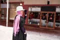 Elegant mature woman in stylish outfit walking near discount clothing store at winter street with shops, wearing headscarf, fedora Royalty Free Stock Photo