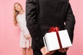 Man in a suit makes a surprise to a woman, gives a bouquet of flowers and a box with a gift, on a pink background of women`s day Royalty Free Stock Photo