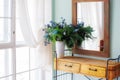 Elegant mirror in wooden frame above fancy console table with flowers