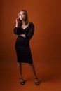 Elegant model wearing black dress and highheel shoes posing on orange background Royalty Free Stock Photo