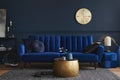 Elegant modern living room interior design with glamour blue velvet sofa, pouf, black metal shelf, poster, plants. Royalty Free Stock Photo