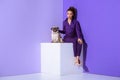 elegant mulatto girl in purple suit sitting on cube with pug, ultra violet Royalty Free Stock Photo