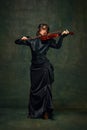 Elegant musician, beautiful young woman in black dress playing violin against dark green vintage background. Symphony