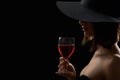 Elegant mysterious woman in a hat holding a glass of red wine on