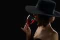 Elegant mysterious woman in a hat holding a glass of red wine on