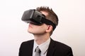 Elegant, neutral man in a black formal suit, wearing a VR Virtual reality Oculus Rift 3D headset, looking upwards to the left