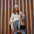 Elegant pretty modern young woman in fashionable spring clothes with a leather black stylish handbag stands near a striped metal Royalty Free Stock Photo