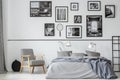 Elegant retro armchair next to king size bed with grey bedding in contemporary bedroom interior with black and white photos Royalty Free Stock Photo