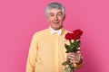 Elegant romantic mature gentleman in formal shirt with bowtie holds red roses, ready for date or birthday, looks directly at