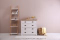 Elegant room interior with stylish chest of drawers, shelving unit and wicker basket