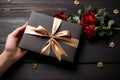 Elegant scene: Female hands with card, gift box on black wooden surface.