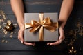 Elegant scene: Female hands with card, gift box on black wooden surface.