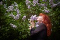 Elegant senior mature Woman in Black Dress by Blooming Lilac Bush at Dusk. A woman with red hair stands poised among