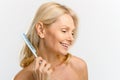 Elegant serene middle-aged blonde woman combing with crest, looks down and laughing cheerfully Royalty Free Stock Photo